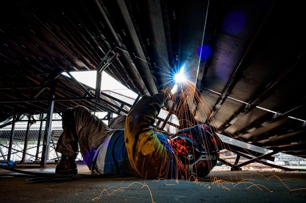 A welder working beneath a steel frame.